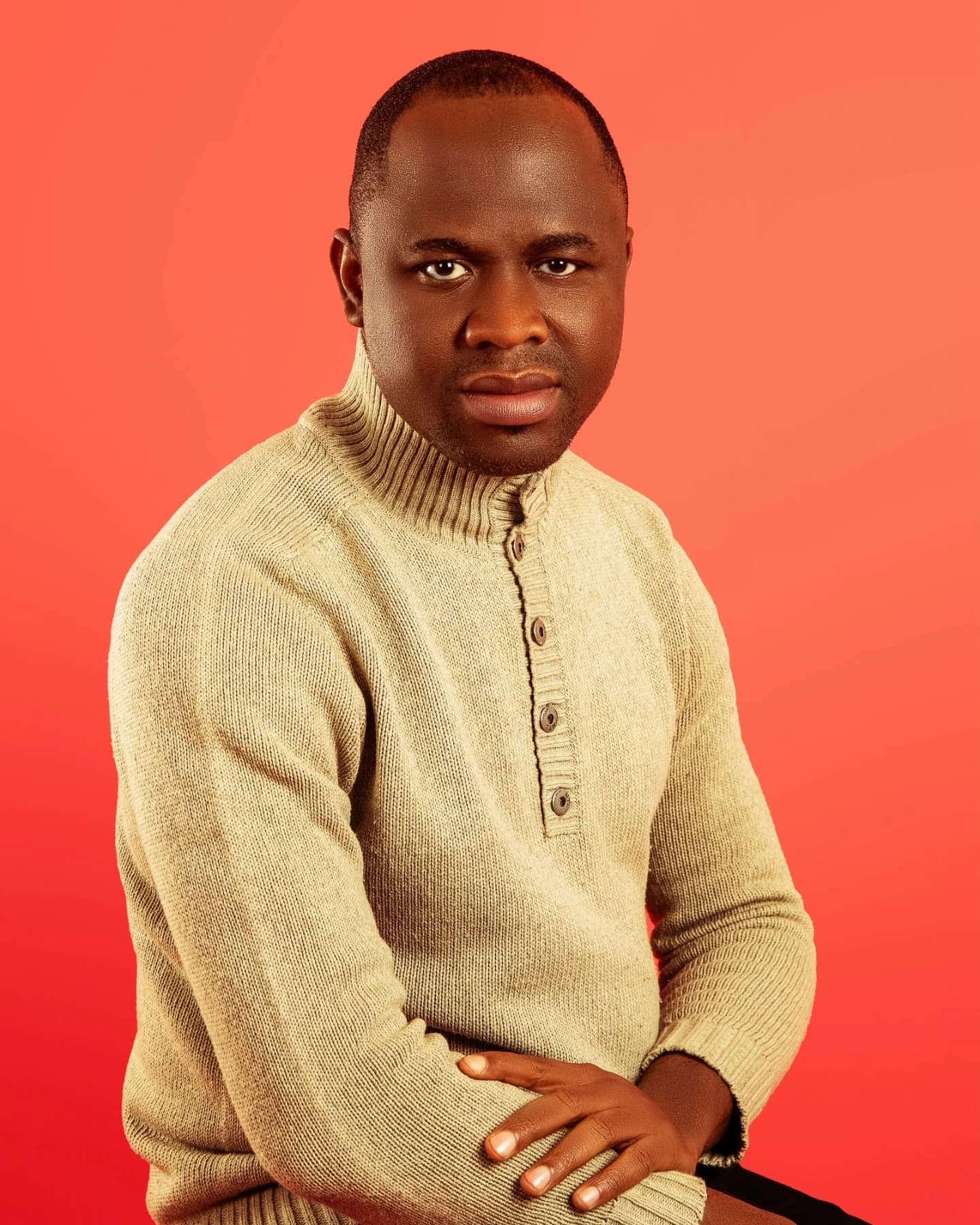 Studio portrait of the photographer behind Precious Diamond, seated in a cream knit jumper against a red backdrop
